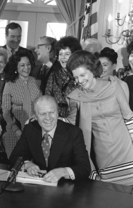 First Lady Betty Ford in the Cabinet Room, congratulating her husband President Gerald R. Ford as he signs the International Year of the Woman proclamation in March 1975, joking to him, "You've come a long way, baby!"