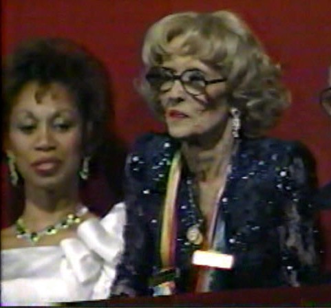 Bette Davis rising to acknowledge a standing ovation during her Kennedy Center honors ceremony, Dianne Carroll behind her, 1987.