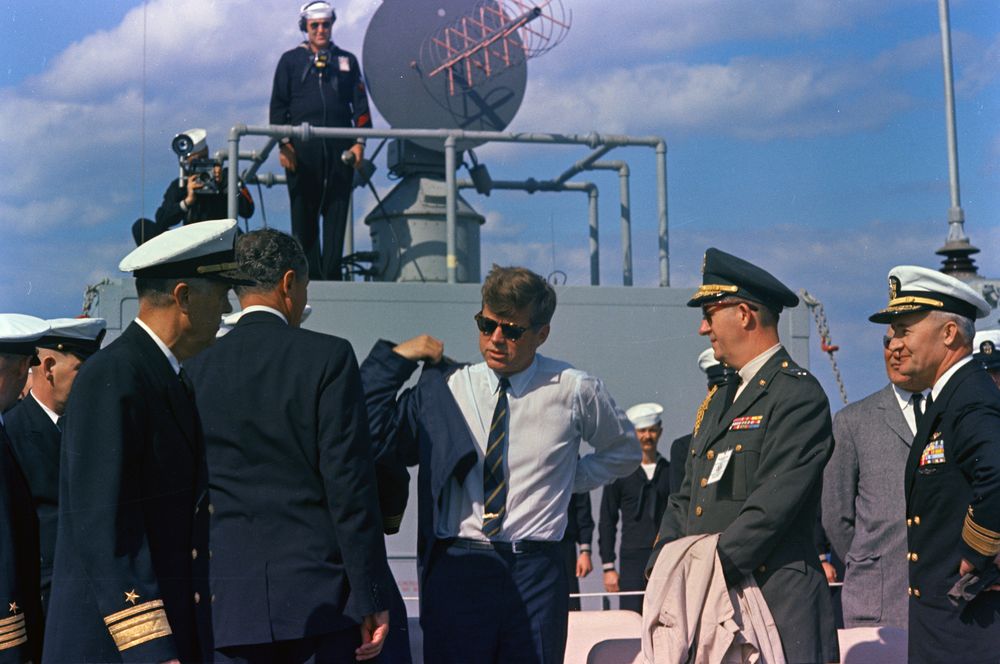 Aboard the USS Observation Island to watch a Polaris Missile launching, JFK tries on the leather jacket given him by the crew.