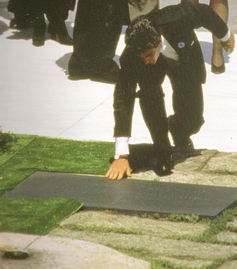 At Jackie's Arlington National Cemetery burial, John kissed his hand and then touched it at the gravestone of his father, besides whom his mother was laid to rest. At Jackie's Arlington National Cemetery burial, John kissed his hand and then touched it at the gravestone of his father, besides whom his mother was laid to rest.