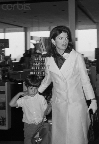 Jackie Kennedy guides her sleepy son through an airport gift shop on their way to Hawaii, 1966. Jackie Kennedy guides her sleepy son through an airport gift shop on their way to Hawaii, 1966.
