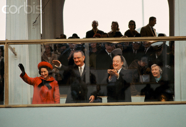 Lady Bird Johnson (left), President Lyndon Johnson (2nd from left), Vice President Hubert Humphrey (2nd from right) and Mrs. Humphrey (right) wave and clap as they watch the inaugural parade from behind protective glass. Washington, D.C., January 1965. --- Image by © Dean Conger/Corbis