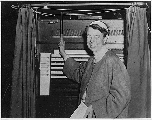 Eleanor Roosevelt posing as she pulls the curtain lever of her voting booth, Hyde Park, New York, 1936.