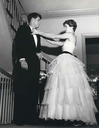 Jackie Kennedy straightens the Senator's tie before their guests arrive. She made an immediately visible change to his public persona by vetting his daily wardrobe.